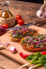 Italian delicious vegan bruschetta with raw chopped tomatoes, chili peppers, spring greens and red onions, herbs and olive oil on a cutting board close-up - rustic style
