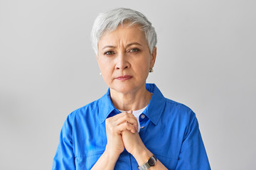 Frustrated worried mature gray haired female holding hands on her chest, having uneasy facial...