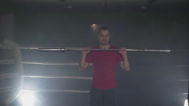 Figher training with barbell in smoky studio in slow motion. Kickboxer training in low light gym in slow motion. Silhouette on dark background