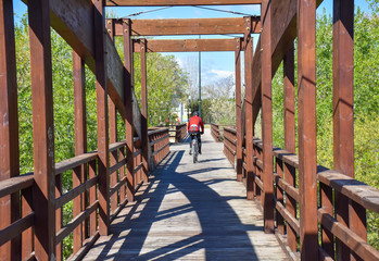 Fototapeta na wymiar cyclist with helmet riding his mountain bike crossing a wooden brown bridge in a sunny day. Rider wears a red sweeter. Horizontal picture