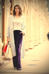 miling beautiful middle aged woman in knitted bright summer coat with shopping bags