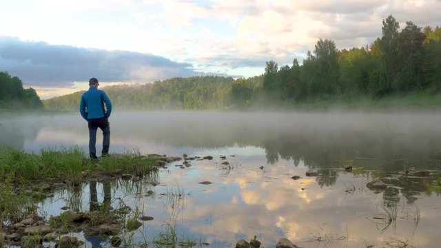 man stands on stone against spreading fog over calm water
