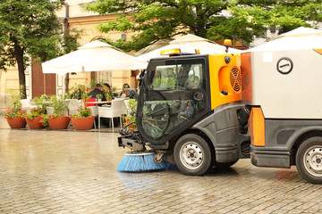 A street sweeper sweeps up a stone pavement with a strong brush in rainy weather. Maintaining clean...