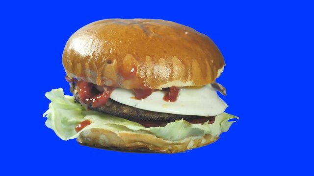American burger with cherry tomatoes cutlets made from natural meat calf or pork with lettuce eggs and a tasty muffin poured over a sauce. Rotates in a circle on an isolated blue background 4k 50 fps
