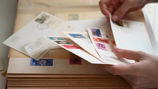 The hands of a young girl are sorting through old envelopes with beautiful color stamps.