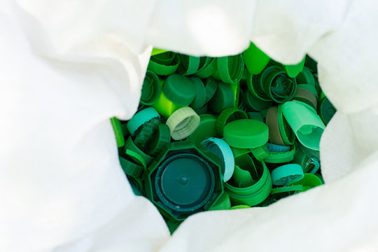 Recycling eco friedly environmenal concept background with colorful green plastic bottle caps in white cellophone package, close up