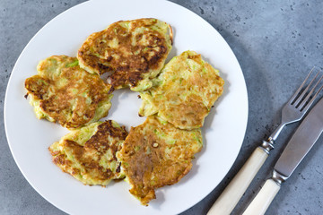 zucchini pancakes on a plate, vegetable pancakes, fork, knife on a gray background