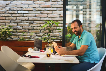 Young man drinking coffee in cafe and using tablet computer, laptop, mobile. Side view.