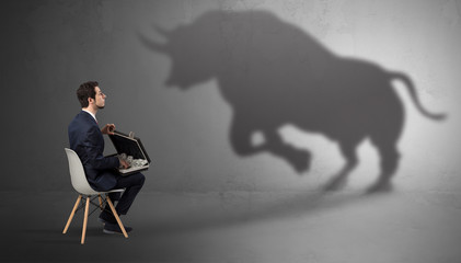 Humble businessman staying and offering stuffs to a huge angry bull shadow
