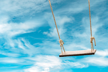 Wooden swing with pastel blue sky and cloud background
