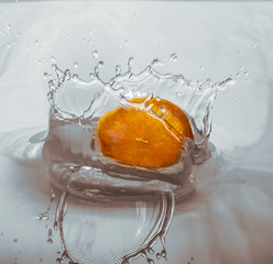 Orangenscheibe taucht spritzend in Wasser ein