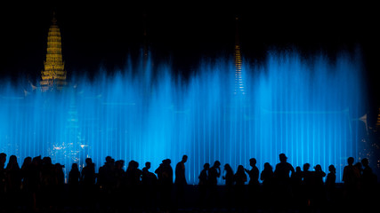 Silhouette of people with blue of fountain curtain in front of Temple.