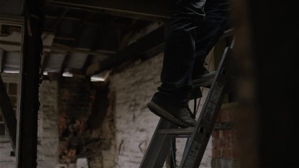 Builder climbs down a ladder from a roof in a derelict building