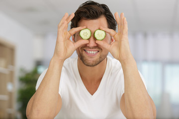 man holding fresh cucumber slices on his face