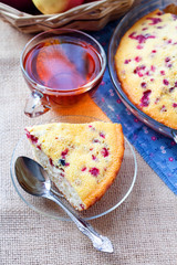 Piece of cowberry pie on glass plate and cup of tea