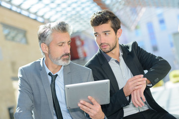 two businessmen are using a table while checking time
