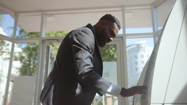 Angry surprised businessman having a failure with a withdrawal operation in a bank. Side view of annoyed bank client trying to take money from invalid ATM machine.