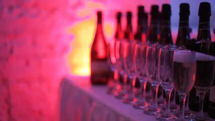 Champagne glasses stand in a row on the table, highlighted with multi-colored light at the party. In the glasses poured champagne. Preglushonny light in the room. Holiday atmosphere in the club