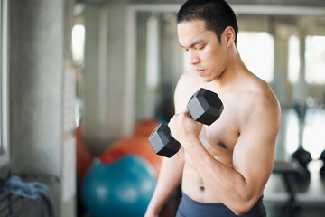 Young Asian man exercising with dumbbells and looking at the dumbbells in the gym. man workout at fitness room. man losing weight training.