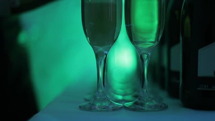 Champagne glasses stand in a row on the table, highlighted with multi-colored light at the party. In the glasses poured champagne. Preglushonny light in the room. Holiday atmosphere in the club