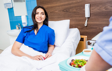 Obraz premium Nurse in medical coat is holding a tray with breakfast for the young female patient.
