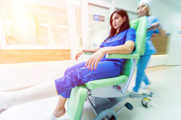 Nurse moves mobile medical chair with patient at hospital. Medical equipment.