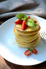 Stack of pancake with strawberries, honey and mint on a white plate