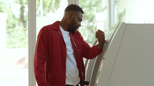 Focused young afro-american man scanning code with a smartwatch withdrawing money from a credit card in the bank at daytime.