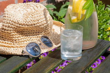 Rest in the garden, fresh cold water hat and sunglasses on a wooden table with flowers in the background