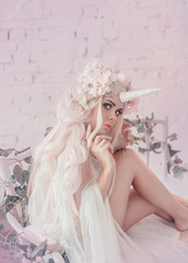 Wonderful creation, the girl is a unicorn in light, white, slightly transparent attire. The background is a bright room that is overgrown with plants, moss, ivy, trees and flowers. Artistic Photo. - obrazy, fototapety, plakaty
