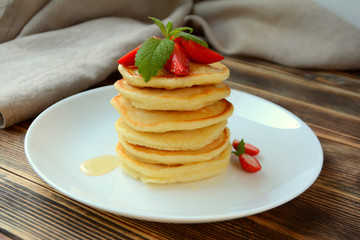 Stack of pancake with strawberries, honey and mint on a white plate