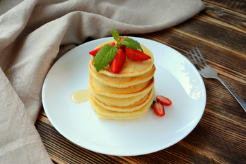 Stack of pancake with strawberries, honey and mint on a white plate