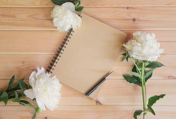 Empty notebook, pen and white peony flowers on wooden table.