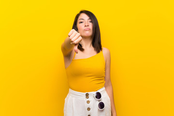 Young Mexican woman over isolated yellow background showing thumb down with negative expression