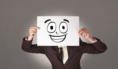 Young student holding a paper with laughing emoticon in front of his face
