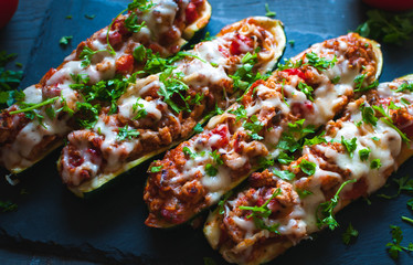 Close-up of stuffed zucchini boats with ground beef, spicy tomato sauce, cheese and fresh parsley, on dark background