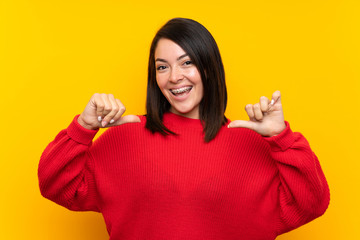 Young Mexican woman with red sweater over yellow wall proud and self-satisfied