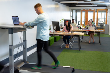 Businessman working on laptop while exercising on treadmill in a modern office