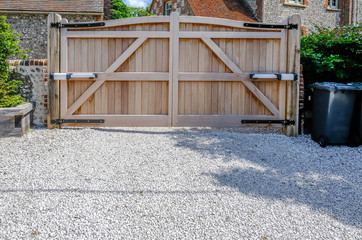 Large wooden entry electric gates with stone driveway.