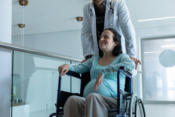 Male doctor pushing pregnant woman on wheelchair in the corridor