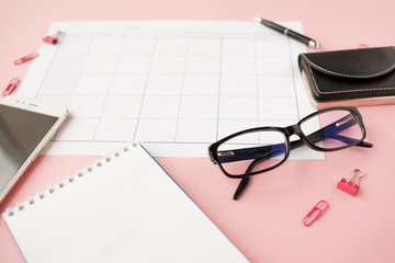 Fototapeta premium Stationery, white smartphone, glasses, pen, wallet, watch, calendar, notebook. Pink background.