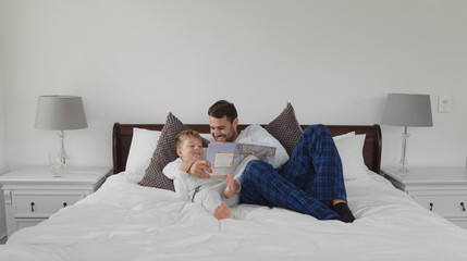 Father and son reading a story book while lying on bed in bedroom