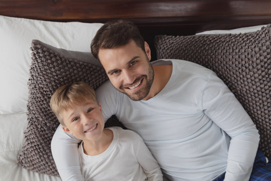 Father and son looking at camera while lying on bed in a comfortable home