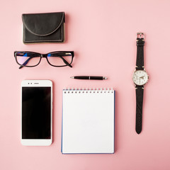 Stationery, white smartphone, glasses, pen, wallet, watch, calendar, notebook. Pink background.