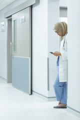 Female doctor in hijab using mobile phone at corridor