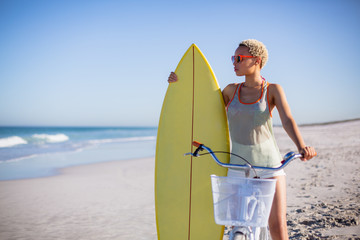 Woman with surfboard sitting on bicycle at beach in the sunshine