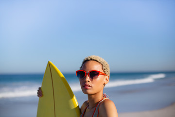 Woman standing with surfboard at beach in the sunshine - obrazy, fototapety, plakaty