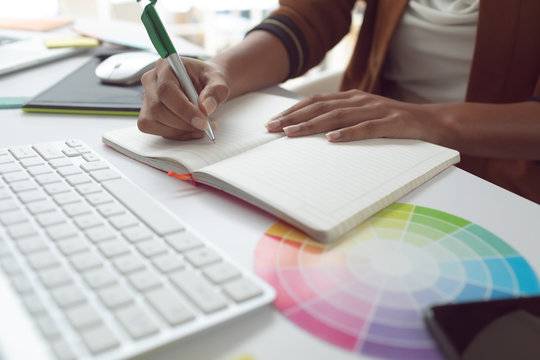 Female graphic designer writing on diary at desk in a modern office