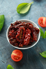 Sun dried tomatoes in white bowl with tomatoes and basil