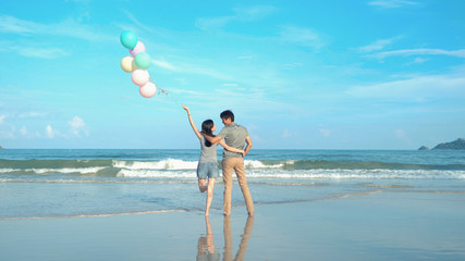 Happy Asian couple holding colorful balloons at the beach during travel trip on holidays vacation...